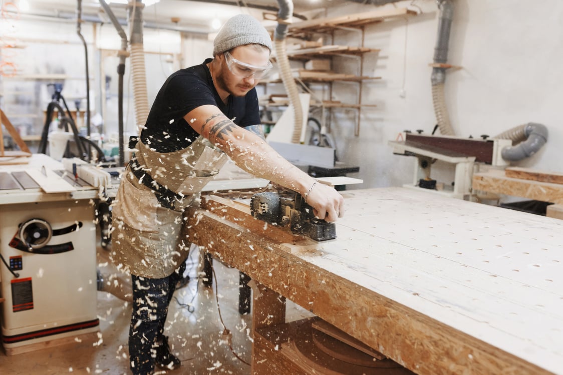 Carpenter working with electric planer on wooden plank in workshop. Craftsman makes own successful small business.